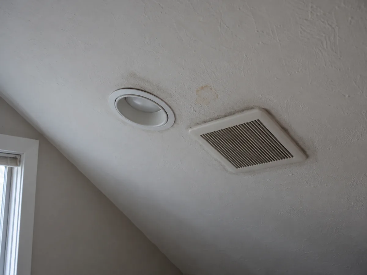 Recessed light and bath fan in a St. Louis Park Cape Cod ceiling where warm air leaks into the attic